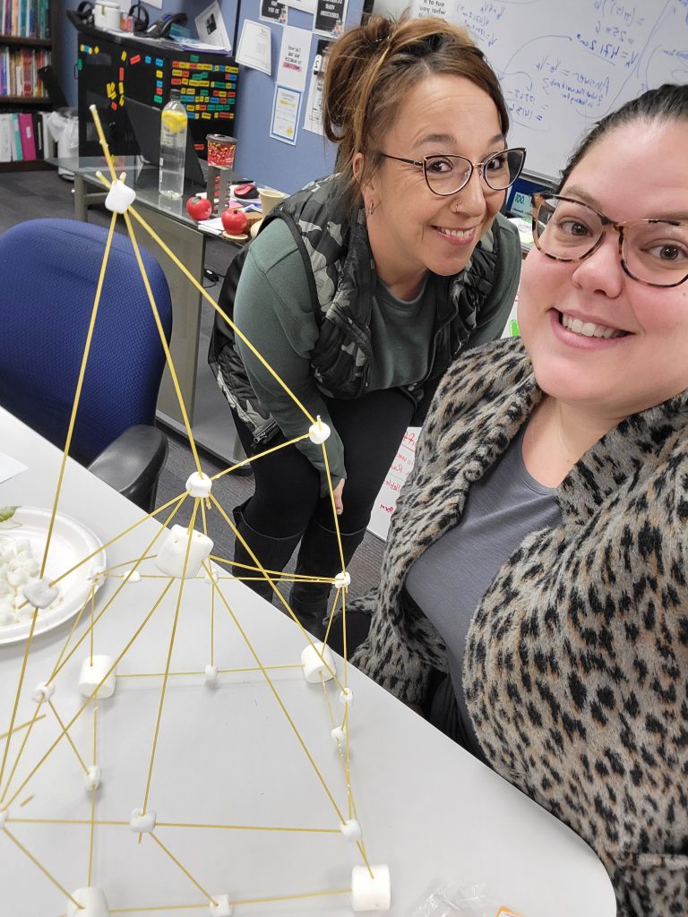 Colleen and Adrianna smile at camera with their spaghetti and marshmallow tower
